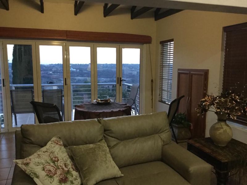 Living room featuring exposed timber beams, tiled flooring, and large folding glass doors opening onto a balcony with expansive views.
