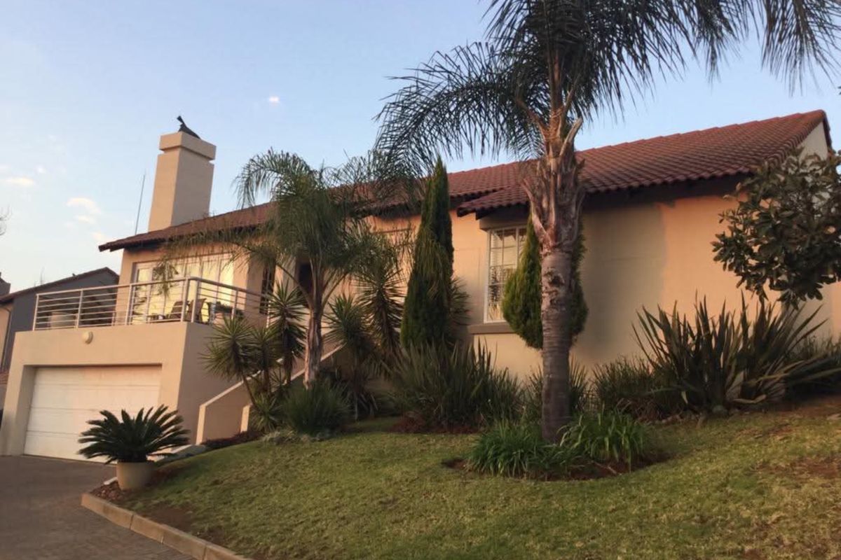 Front elevation of a townhouse featuring a tiled roof, chimney, integrated garage, and an elevated balcony with metal railing, set within a landscaped garden.