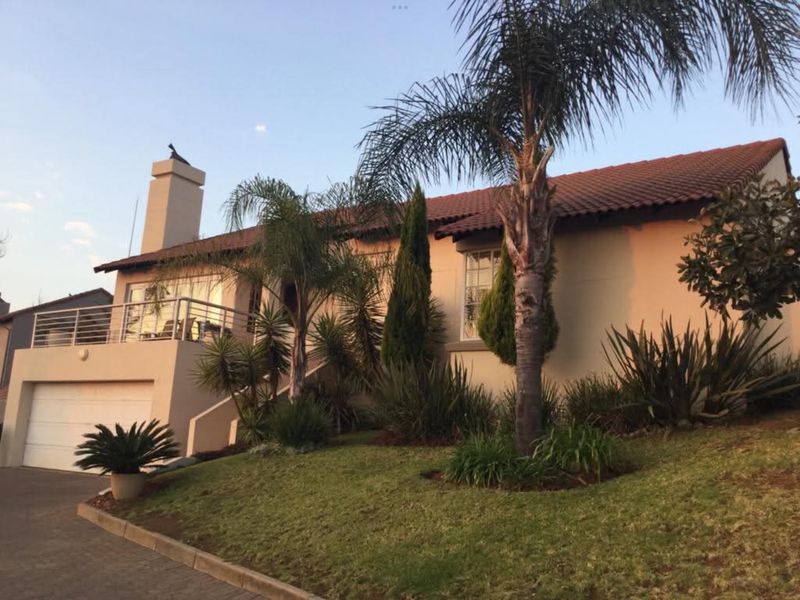 Front elevation of a townhouse featuring a tiled roof, chimney, integrated garage, and an elevated balcony with metal railing, set within a landscaped garden.
