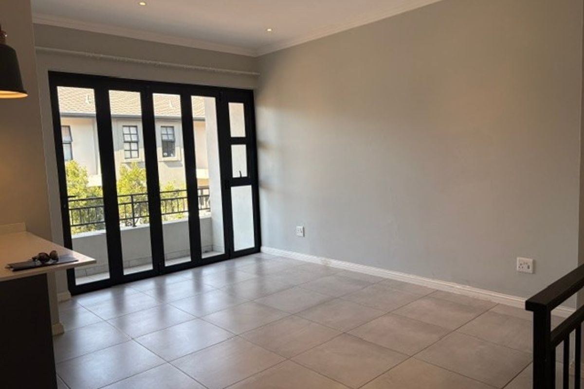 Spacious, light-filled living area featuring neutral tiled flooring, recessed downlights, and large black aluminium folding doors leading to a private balcony.