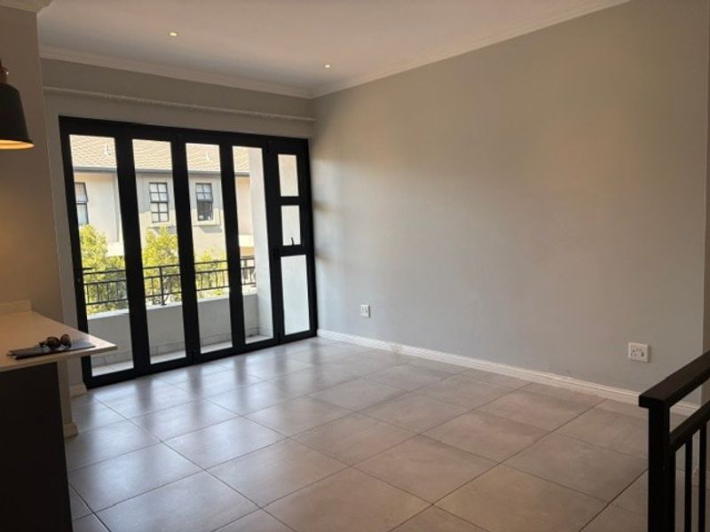 Spacious, light-filled living area featuring neutral tiled flooring, recessed downlights, and large black aluminium folding doors leading to a private balcony.