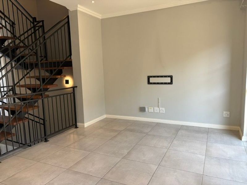 An empty living room featuring modern tiled flooring, a staircase with a metal balustrade, and wall-mounted TV infrastructure.