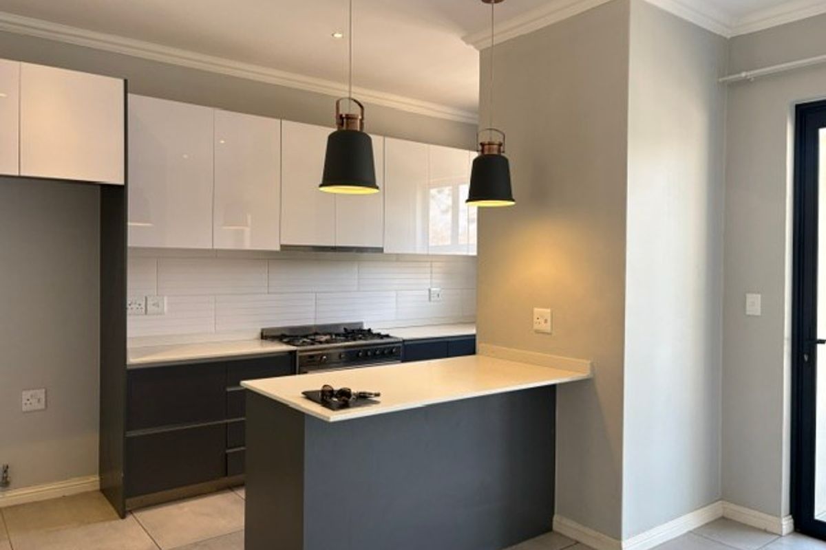 Modern kitchen featuring sleek two-tone cabinetry, stone countertops, a gas stove with extractor, and stylish pendant lighting over a breakfast bar.