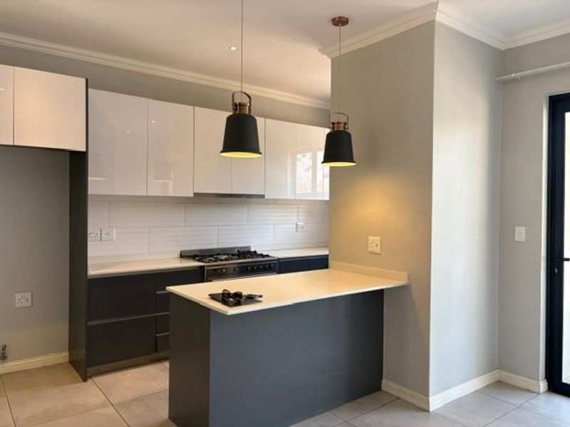 Modern kitchen featuring sleek two-tone cabinetry, stone countertops, a gas stove with extractor, and stylish pendant lighting over a breakfast bar.
