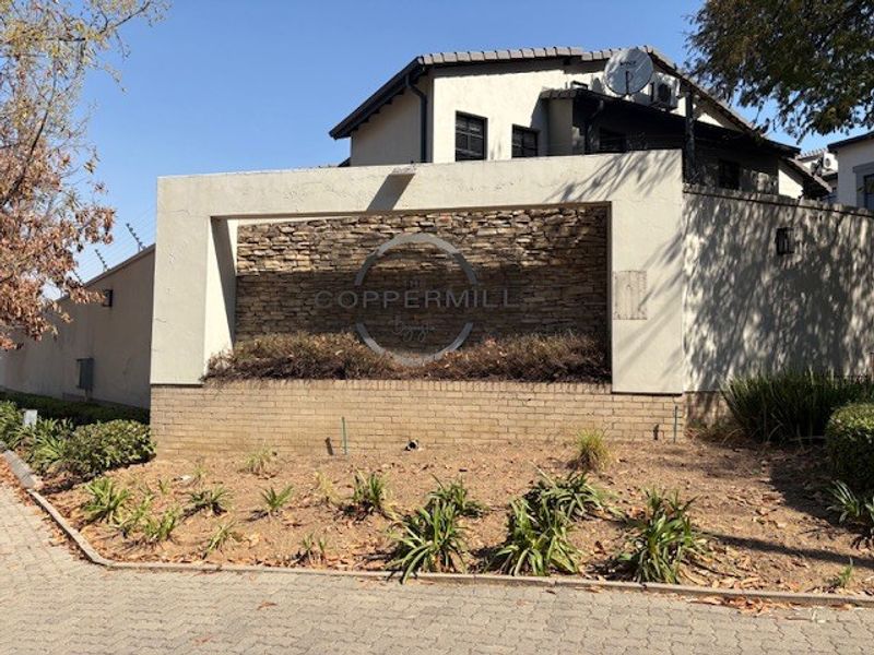 The entrance facade of The Coppermill complex, featuring a stone-clad signage wall, brick boundary wall, and paved driveway access.