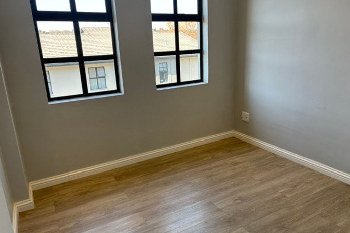 A bright, empty bedroom featuring modern laminate flooring and black-framed windows, providing a clean and neutral space ready for personalization.