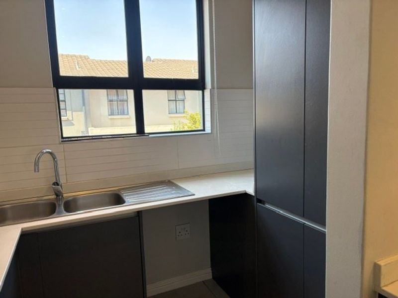 A modern kitchen area featuring dark cabinetry, stone countertops, a double sink with a mixer tap, and a clean subway tile backsplash.