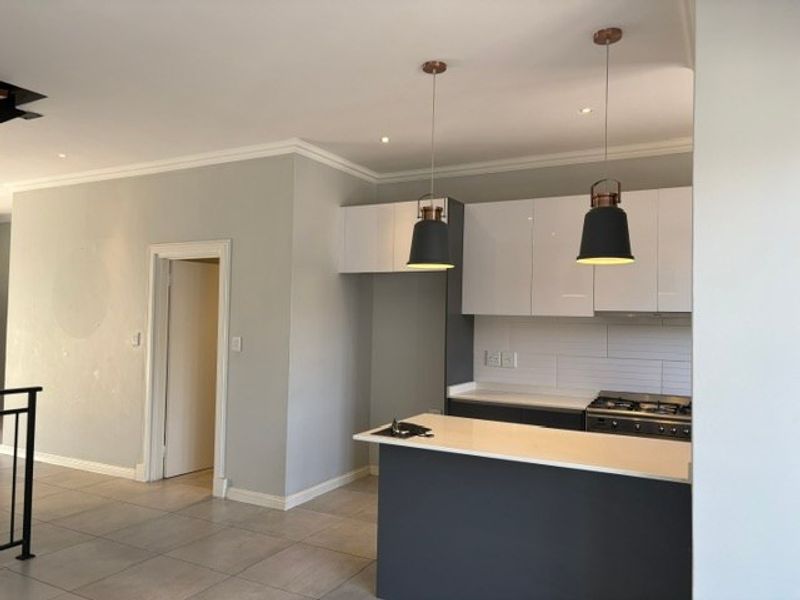 Modern open-plan kitchen featuring sleek cabinetry, stone countertops, a gas hob, and stylish pendant lighting, seamlessly integrated into the living space.