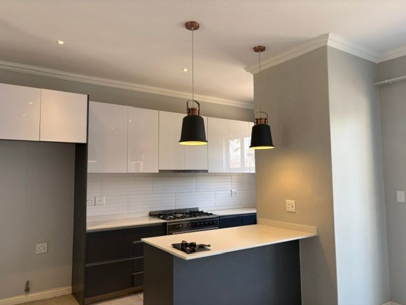 Modern kitchen featuring high-gloss cabinetry, stone countertops, a gas hob with extractor, and a functional breakfast nook with stylish pendant lighting.