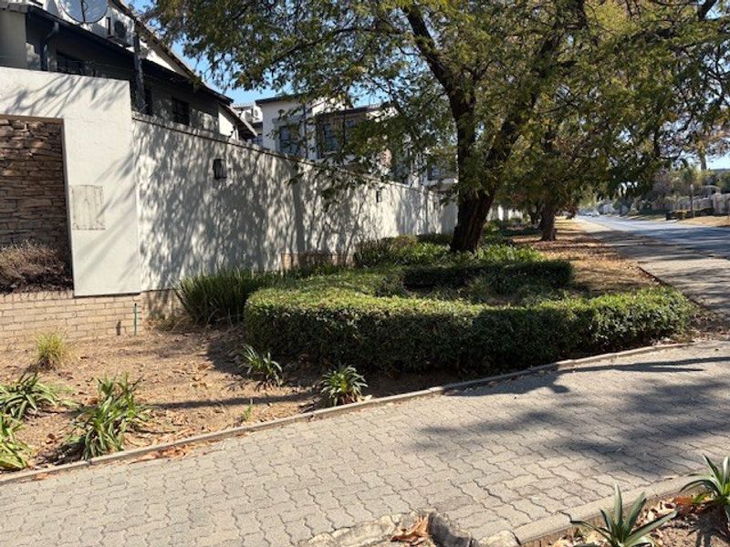 A view of the property boundary wall featuring stone cladding, adjacent to a paved sidewalk and landscaped verge with mature trees.