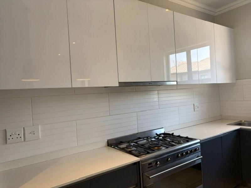 Modern kitchen featuring high-gloss white cabinetry, a gas hob with extractor fan, and a clean tiled backsplash.