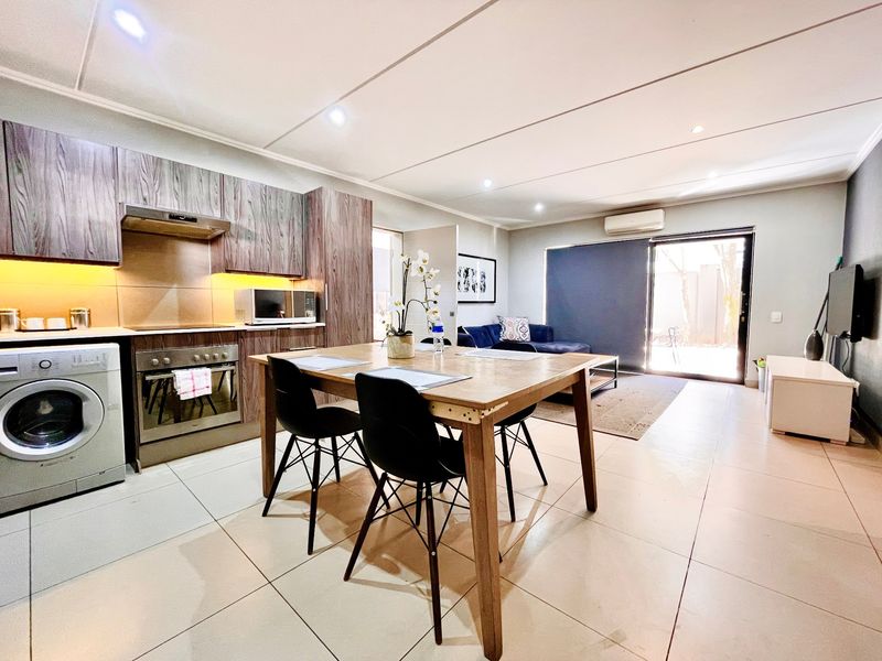 Open-plan living area featuring a modern kitchen with built-in appliances, tiled flooring, and direct access to an outdoor space through a sliding glass door.