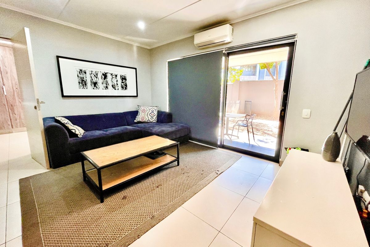 A well-maintained living room featuring tiled flooring, a wall-mounted air conditioning unit, and a sliding glass door providing access to an outdoor area.