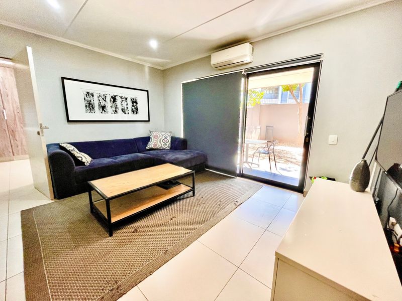 A well-maintained living room featuring tiled flooring, a wall-mounted air conditioning unit, and a sliding glass door providing access to an outdoor area.