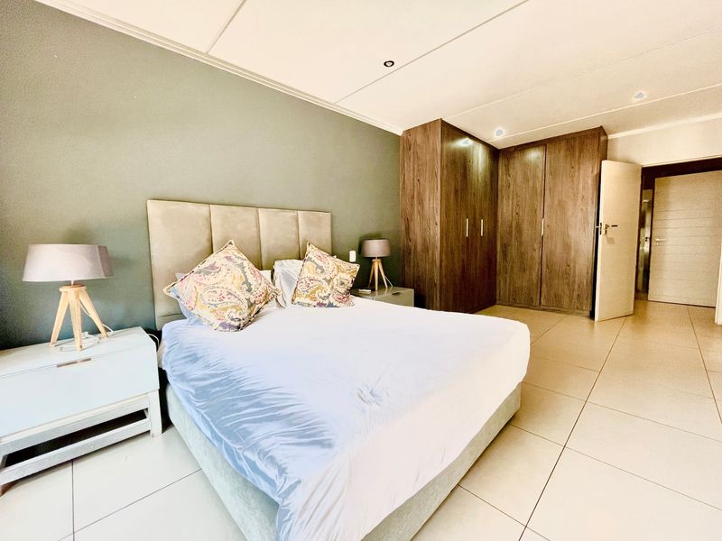 Spacious bedroom featuring neutral tiled flooring, built-in wooden cupboards, and modern recessed lighting, creating a clean and functional living space.