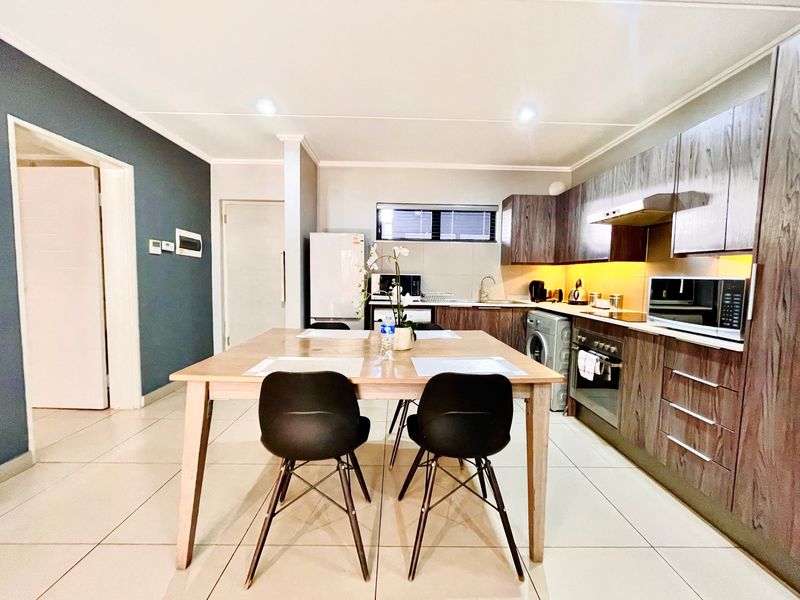 Modern open-plan kitchen and dining area featuring dark wood cabinetry, integrated appliances, tiled flooring, and recessed lighting.