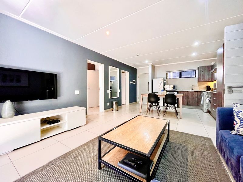 Modern open-plan living area featuring tiled floors, recessed lighting, and a functional kitchen with built-in cabinetry and appliances.