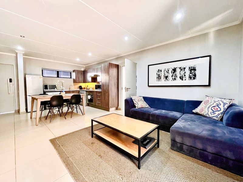 Open-plan living area featuring a modern kitchen with wood-finish cabinetry, tiled floors, and recessed lighting, seamlessly flowing into a comfortable lounge space.