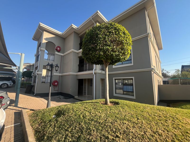 Front elevation of a multi-story apartment complex featuring paved driveway, landscaped garden, and private balconies with security gates.