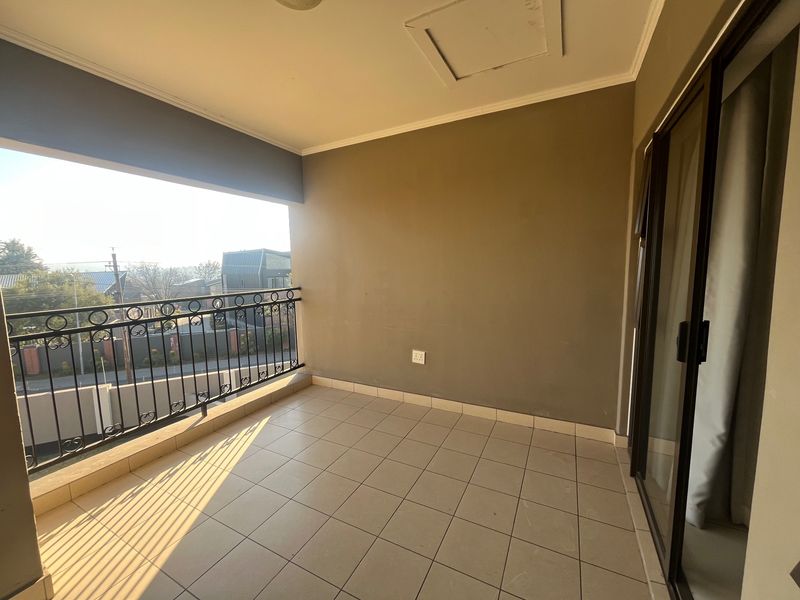 A spacious, empty balcony featuring tiled flooring, a wrought iron balustrade, and sliding glass door access, offering an open outdoor area.