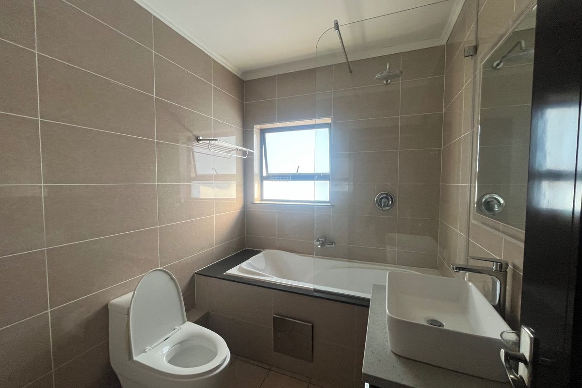 Modern bathroom featuring a built-in bathtub with glass shower screen, vessel sink on a stone vanity, and neutral wall tiling.