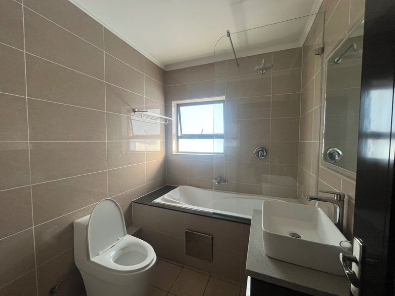 Modern bathroom featuring a built-in bathtub with glass shower screen, vessel sink on a stone vanity, and neutral wall tiling.