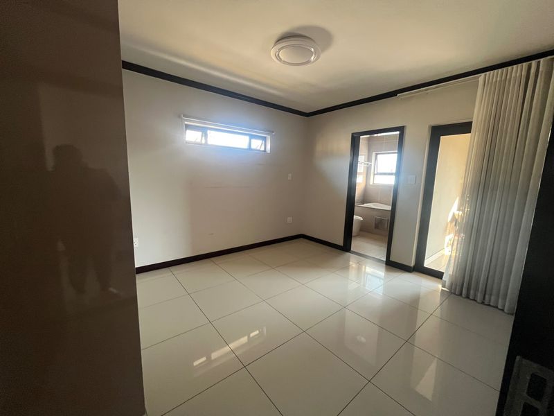 A bright, empty bedroom featuring neutral tiled flooring, modern skirting, and direct access to an en-suite bathroom and a private balcony area.