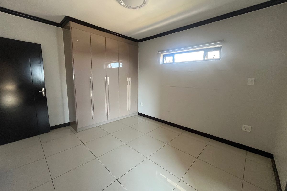 A clean, empty bedroom featuring neutral tiled flooring, built-in cupboards, and a high-level window, providing a blank canvas for personalization.