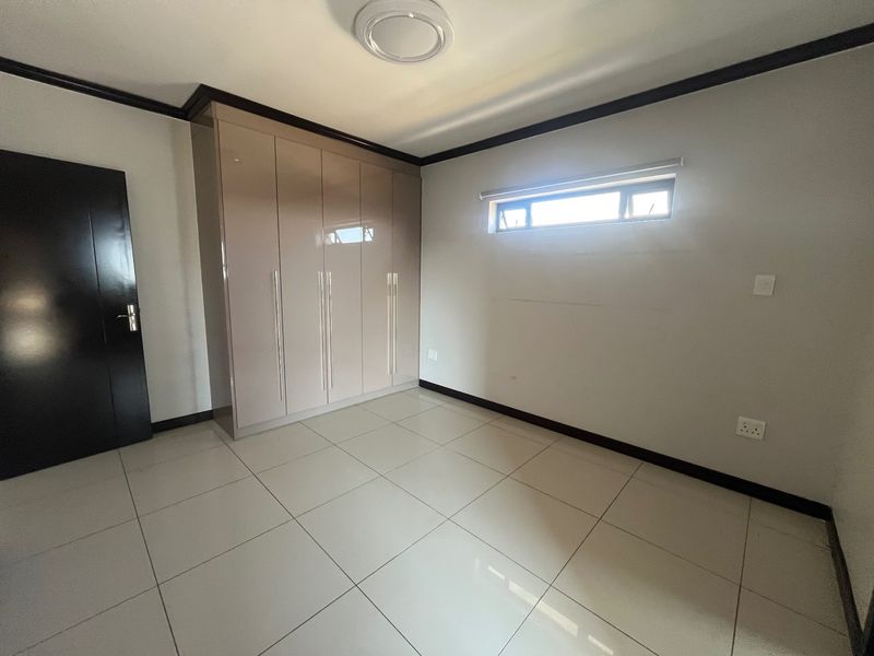 A clean, empty bedroom featuring neutral tiled flooring, built-in cupboards, and a high-level window, providing a blank canvas for personalization.