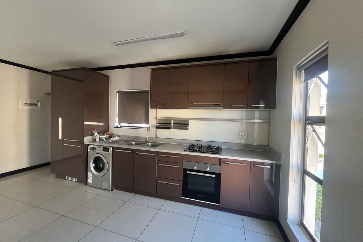 Modern kitchen featuring dark brown cabinetry, built-in gas hob, electric oven, and integrated laundry plumbing with tiled flooring.