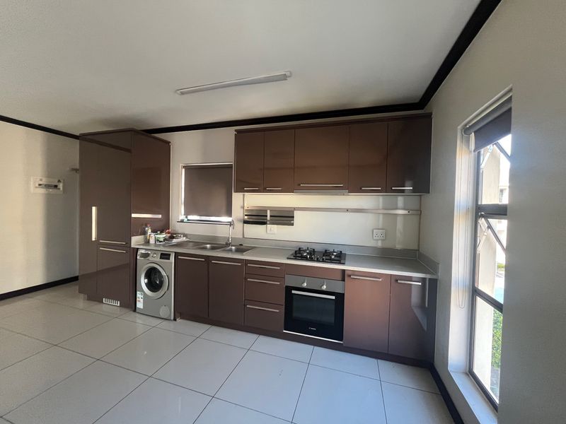 Modern kitchen featuring dark brown cabinetry, built-in gas hob, electric oven, and integrated laundry plumbing with tiled flooring.
