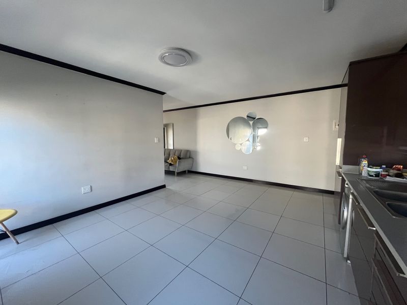 Open-plan living and kitchen area featuring neutral tiled flooring, dark cabinetry, and a clean, minimalist layout suitable for modern living.