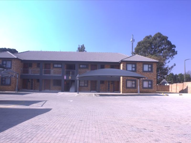 Front view of a multi-story brick apartment complex featuring a paved parking area and covered carports.