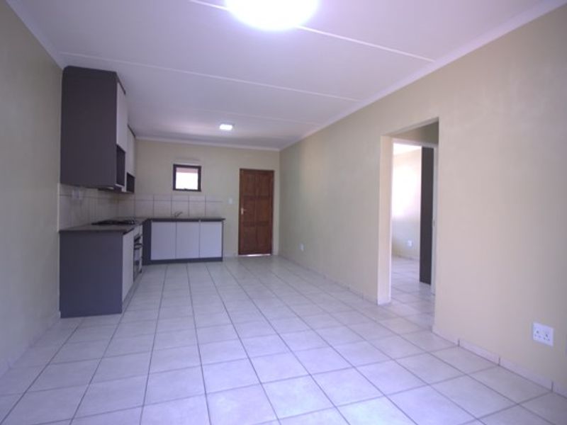 An open-plan living and kitchen area featuring tiled flooring, modern two-tone cabinetry, and a built-in oven and hob.