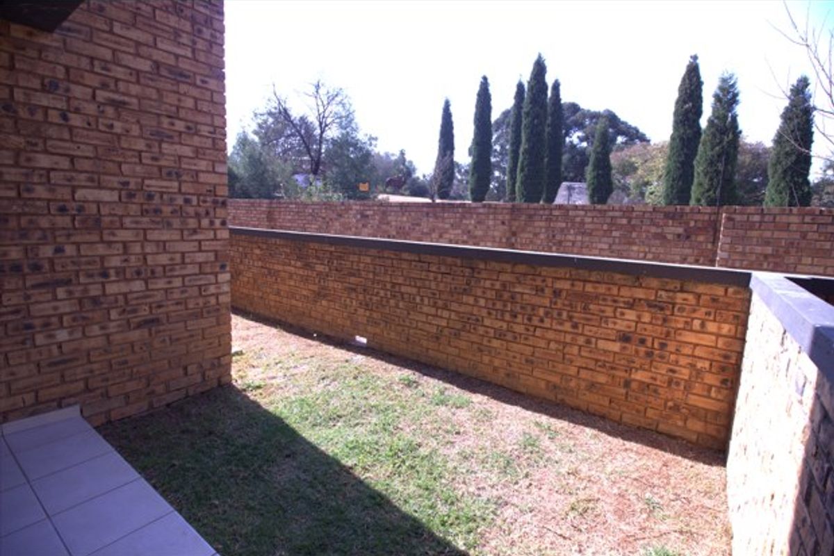 A private rear courtyard featuring a brick boundary wall, a small lawn area, and a tiled patio section.