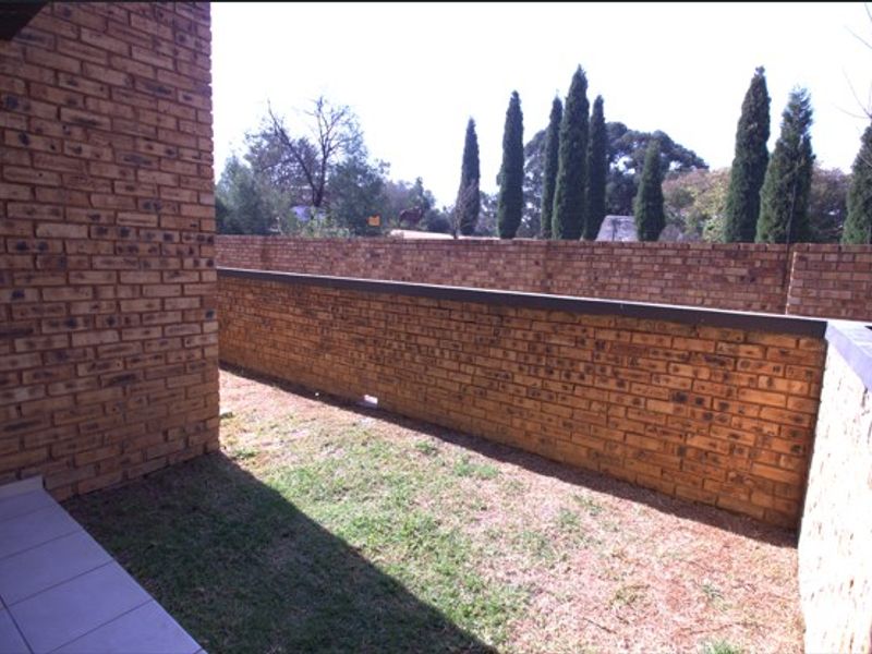 A private rear courtyard featuring a brick boundary wall, a small lawn area, and a tiled patio section.
