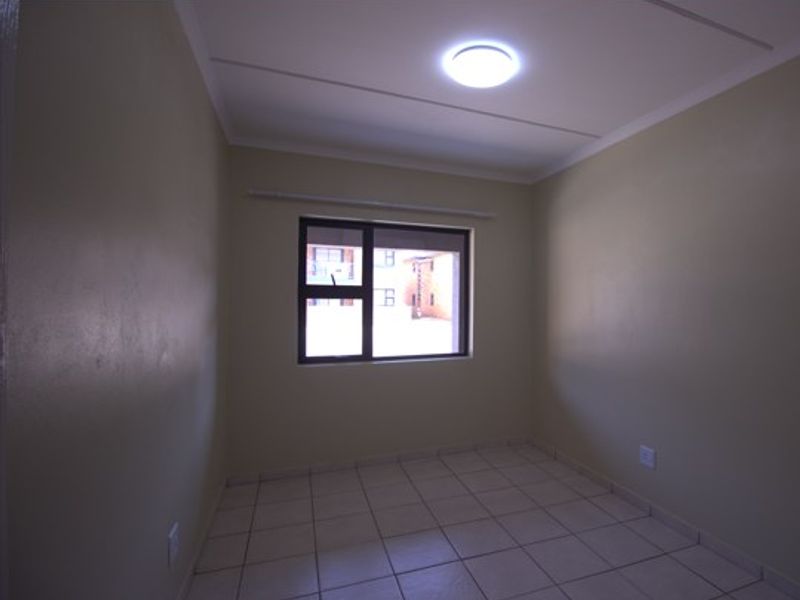 A clean, empty bedroom featuring neutral wall paint, tiled flooring, and an aluminium-framed window providing natural light.
