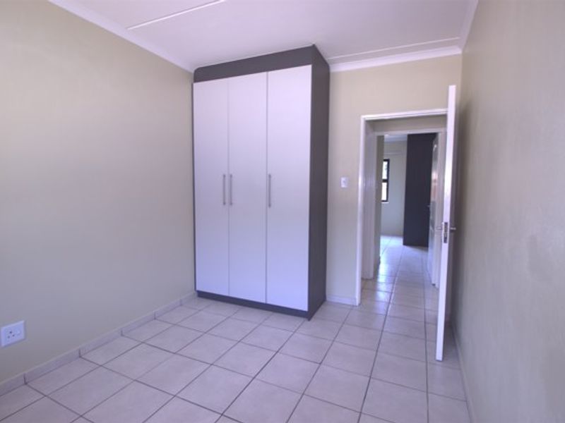 A clean, empty bedroom featuring neutral wall tones, tiled flooring, and a modern built-in wardrobe with a contrasting frame.