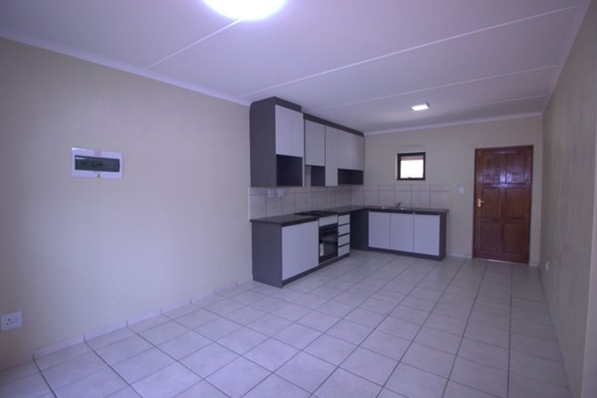 A clean, empty kitchen featuring modern two-tone cabinetry, tiled flooring, a built-in oven and hob, and a tiled backsplash.