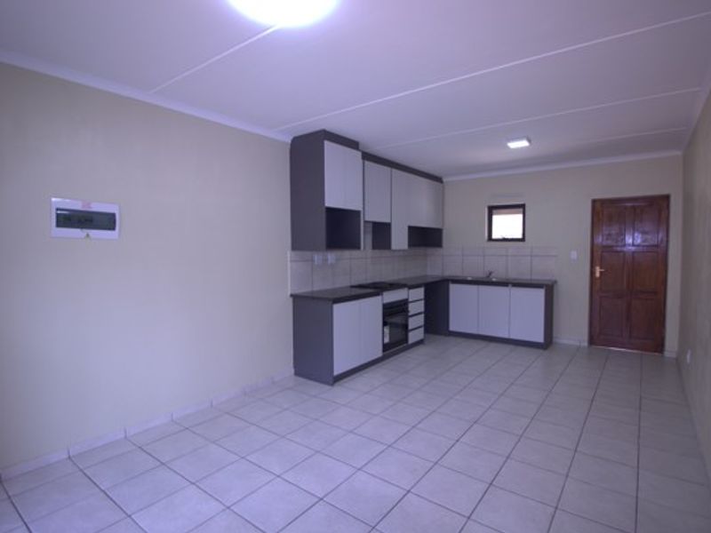 A clean, empty kitchen featuring modern two-tone cabinetry, tiled flooring, a built-in oven and hob, and a tiled backsplash.
