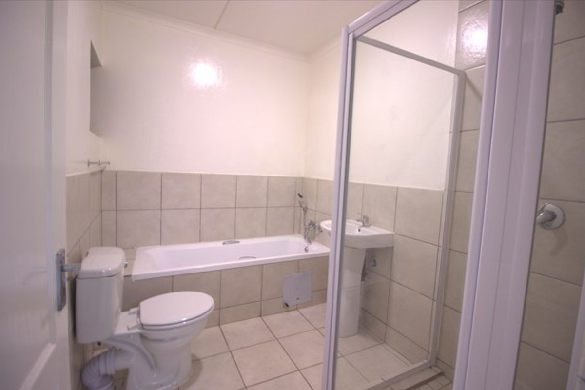 A functional bathroom featuring a bathtub, pedestal sink, toilet, and a separate shower enclosure with neutral wall and floor tiling.
