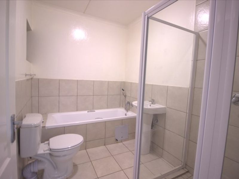 A functional bathroom featuring a bathtub, pedestal sink, toilet, and a separate shower enclosure with neutral wall and floor tiling.