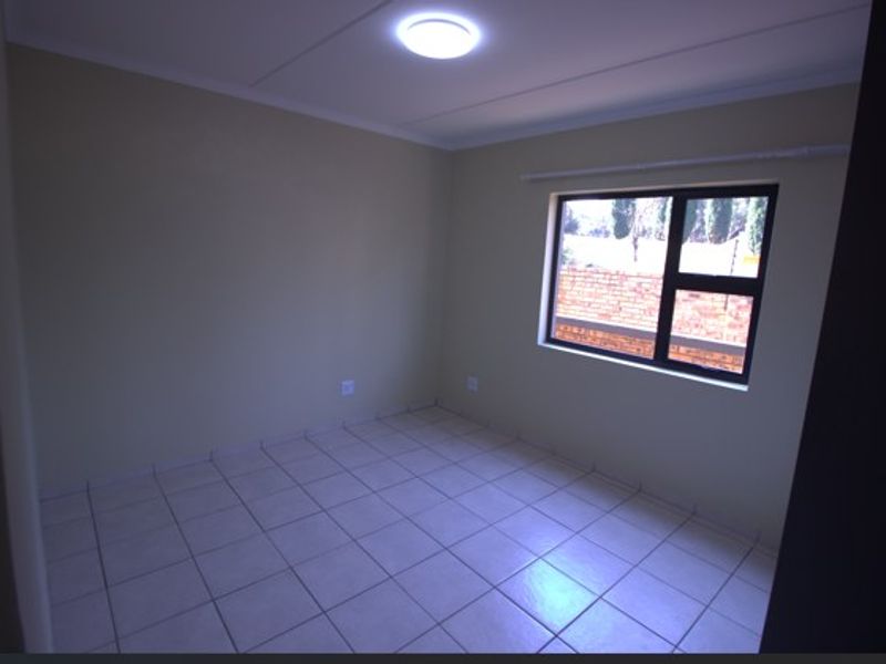 An empty bedroom featuring neutral wall paint, tiled flooring, and an aluminium-framed window with a curtain rail.