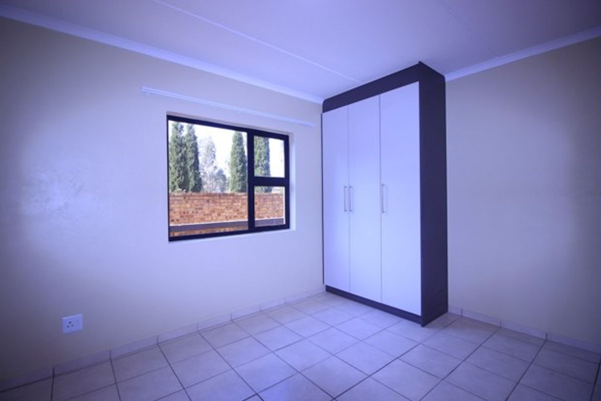 A clean, empty bedroom featuring neutral tiled flooring, a modern built-in wardrobe, and an aluminium-framed window providing natural light.
