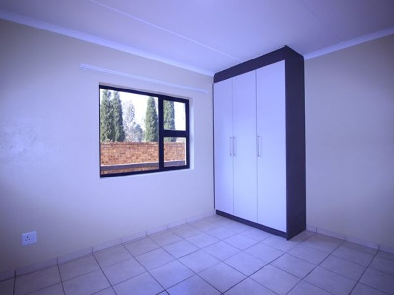 A clean, empty bedroom featuring neutral tiled flooring, a modern built-in wardrobe, and an aluminium-framed window providing natural light.