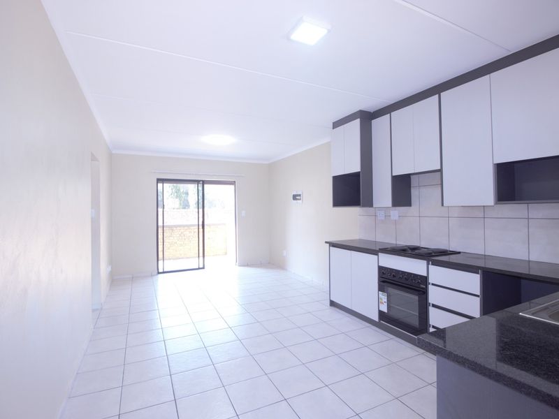 Open-plan kitchen and living area featuring modern cabinetry, granite countertops, built-in oven, and tiled flooring, leading to a private balcony.