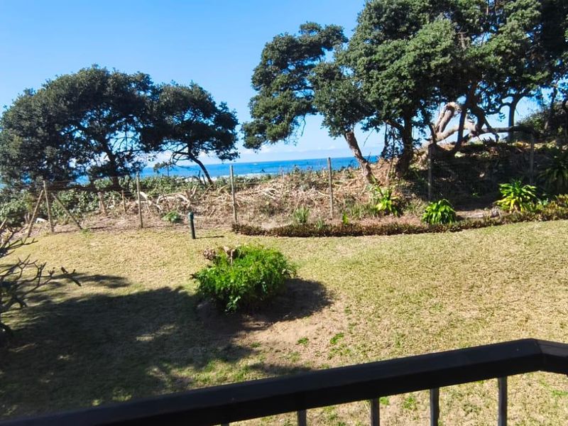 A scenic view of the coastal landscape and garden, captured from an elevated balcony with a metal railing.