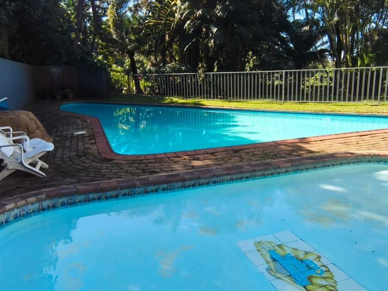 Outdoor pool area featuring a swimming pool and integrated spa, surrounded by brick paving, metal fencing, and a retaining wall.