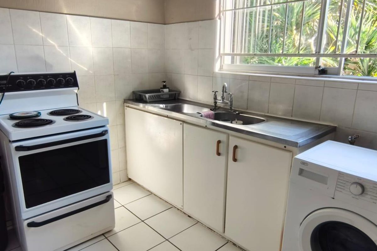 A functional kitchen featuring tiled splashbacks, stainless steel sink, and built-in cabinetry, with security bars on the window providing natural light.