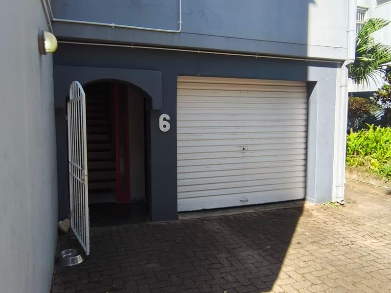 Exterior view of a residential garage featuring a white roller shutter door and paved driveway access.